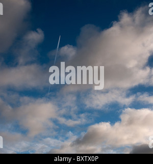 Jet and vapourtrail against a blue and cloudy sky. Stock Photo