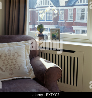 Cream cushion on beige armchair in front of window above radiator with white cover Stock Photo