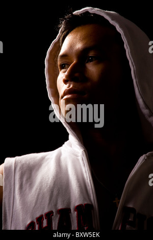 A young ethnic Hip Hop male artist wearing a white Hoodie stands posed looking away from camera with Rembrandt styled lighting Stock Photo