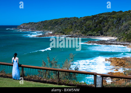 A young woman watches people surfing from cliff top vantage point at Point Perry Coolum Beach Queensland Australia Stock Photo