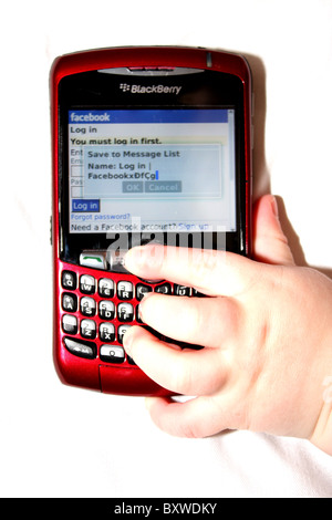 A white Caucasian baby toddlers hand using a red Blackberry mobile phone device to type a message. Stock Photo