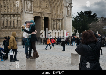 Two young women standing on a bollard hugging whilst having their picture taken in front of Notre Dame Cathedral, Paris. Stock Photo
