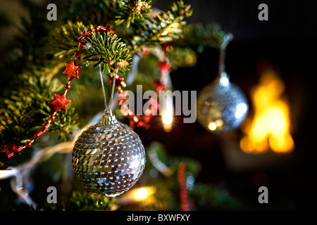 Disco mirror ball decorations hanging from a Christmas tree in front of a fire on Christmas eve Stock Photo