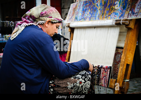 A woman uses a loom to weave a Turkish carpet at the Arastar Bazaar, a small bazaar next to the Sultanahment Camii (Blue Mosque) in Istanbul, Turkey. Stock Photo