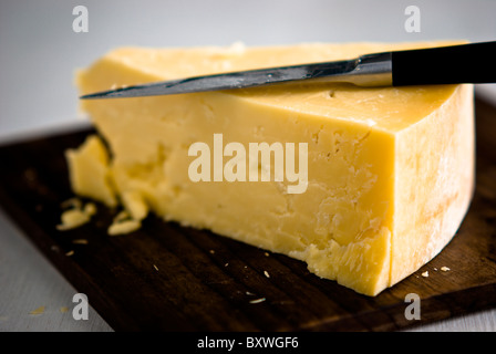 Wedge of cheddar cheese, being cut on wooden cheeseboard Stock Photo