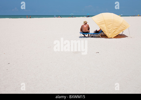 USA, Florida, St. Petersburg, Man sits sunbathing on white sand beach along Gulf of Mexico on summer morning Stock Photo