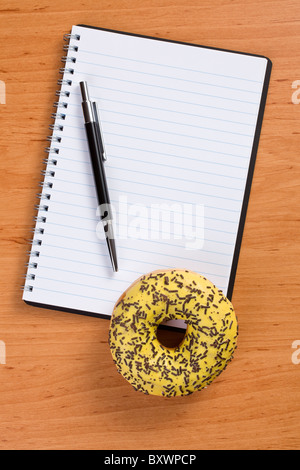 sweet doughnut and spiral notebook on wooden table Stock Photo