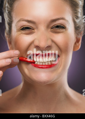 white blonde woman biting a chili pepper Stock Photo