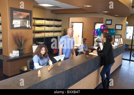 Patient talks to dentist at clinic's reception desk before leaving after her appointment as staffers work at computer stations Stock Photo