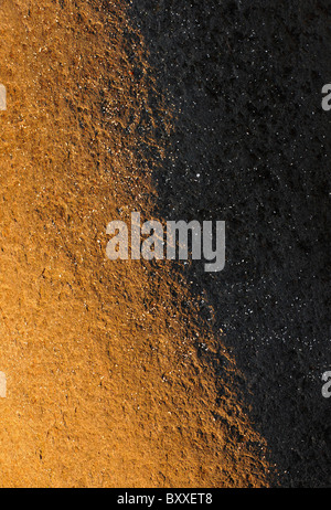 Low evening sun casting warm light and shadow on a rock with white grains of sand. Stock Photo