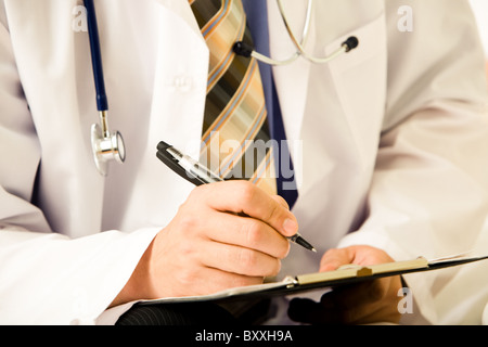 Close-up of doctor’s hands holding pen over paper ready to prescribe pills to patient Stock Photo
