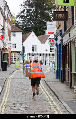 A postman in a red hi-viz jacket runs to deliver a parcel in Guildford, Surrey, England. Stock Photo