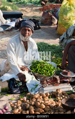 Muslim man weighing green chillis at a vegetable market in Puttaparthi, Andhra Pradesh, India Stock Photo