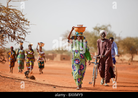 Women arrive in the town of Djibo, Burkina Faso, on foot, carrying their wares on their heads in traditional African fashion. Stock Photo