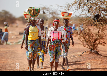 Women arrive in the town of Djibo, Burkina Faso, on foot, carrying their wares on their heads in traditional African fashion. Stock Photo