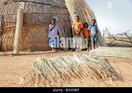 In the Fulani village of Jolooga in northern Burkina Faso, children stand outside a traditional house made of straw. Stock Photo