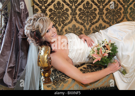 beautiful white bride lying on modern damask couch Stock Photo