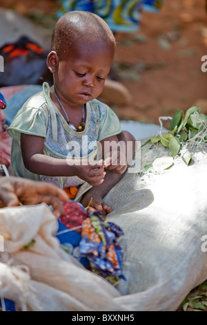 In the town of Djibo in northern Burkina Faso, a child plays quietly as her mother sells greens in the market. Stock Photo