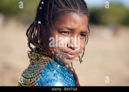 In a seasonal Fulani village in northern Burkina Faso, reflections from the sequins of a young woman's shawl dance on her face. Stock Photo