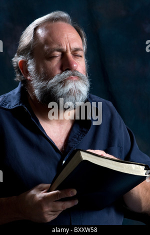 Bearded man praying while holding Holy Bible. Stock Photo