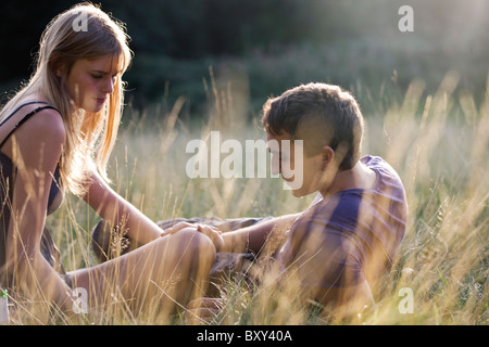 A young couple sitting in the grass, mans hand on the womans knee Stock Photo