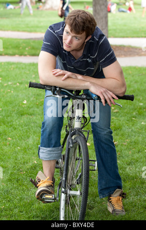 Pensive young man resting his arms on his bicycle handlebars Stock Photo