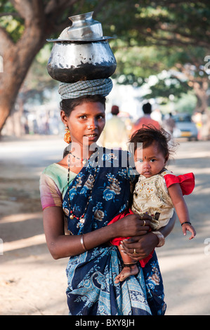 Poor lower caste Indian woman with baby carrying a pot of rice on her head. Andhra Pradesh, India Stock Photo