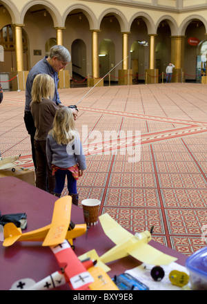 An Elderly man shows his two preteen granddaughters the remote control functions of a model airplane - USA Stock Photo
