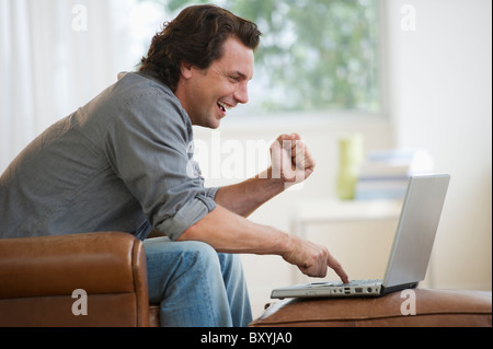 Man on armchair using laptop and laughing Stock Photo