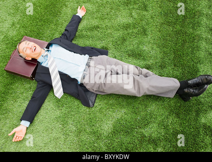 Happy businessman lying on lawn with briefcase under head Stock Photo