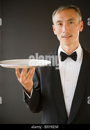 Waiter wearing bow tie and holding tray, studio shot Stock Photo