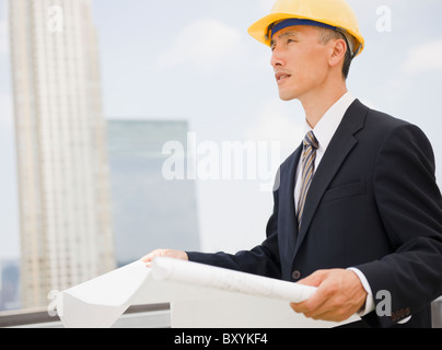 Engineer holding plans, wearing protective helmet and looking away Stock Photo