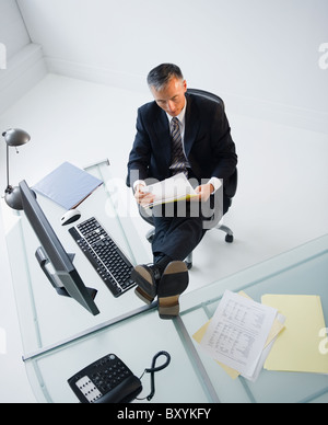 Businessman reading documents in office with feet on desk Stock Photo