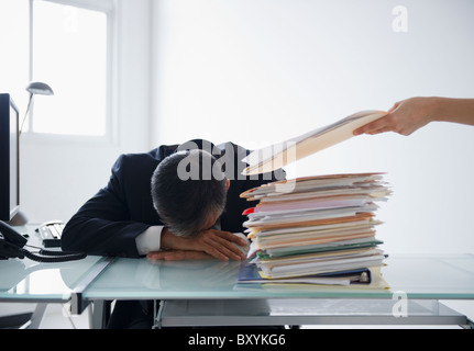 Businessman with head on desk and pile of documents in front of him Stock Photo