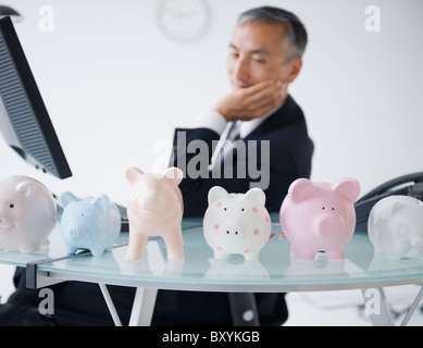 Businessman looking at piggybanks standing on desk Stock Photo