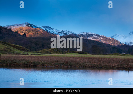 The rising sun lights up the snow topped fells at Elterwater in the Great Langdale Valley, Lake district Stock Photo
