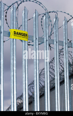Danger sign warning of concertina razor wire mounted onto galvanized steel  pointed fence. Stock Photo