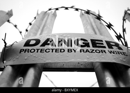 Danger sign warning of concertina razor wire mounted onto galvanized steel  pointed fence. Stock Photo