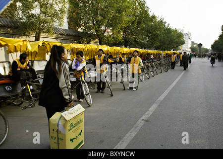 CHINA, BEIJING: Pedicab drivers with yellow canopied bicycle rickshaws wait for customers in the Hutong neighborhood of Beijing. Stock Photo