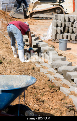 A construction worker lays concrete blocks for a retaining wall. Stock Photo