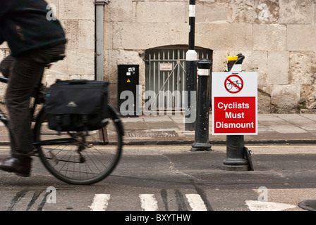 Cyclist riding past a sign ordering cyclists to dismount in Broad Street, Oxford, Oxfordshire, UK.