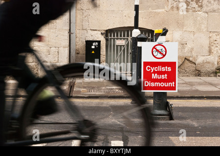 Cyclist riding past a sign ordering cyclists to dismount in Broad Street, Oxford, Oxfordshire, UK.