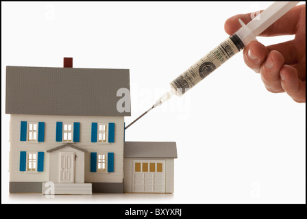 Girls hand injecting money into house Stock Photo