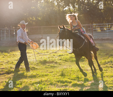 Trainer assisting girl riding horse in paddock