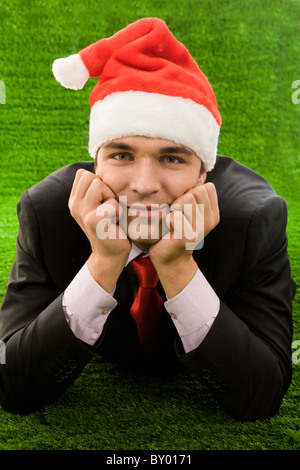 Businessman in santa cap touching his face by hands while relaxing on green grass Stock Photo