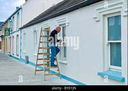 Man paints windows of a house in Chapel Street, Kilkee, County Clare, West of Ireland Stock Photo