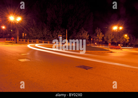 roundabout at night illuminated by streetlights and the headlights of cars Stock Photo
