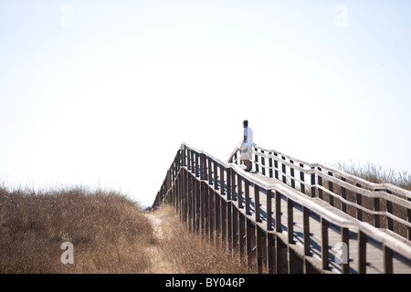 A man standing on a wooden bridge over sand dunes Stock Photo
