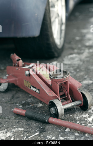 A close up of a red hydraulic trolley jack next to a car on an icy driveway with the handle detached. Stock Photo