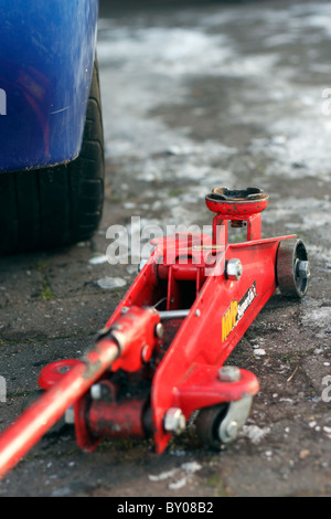 A close up of a red hydraulic trolley jack next to a car on an icy driveway. Stock Photo